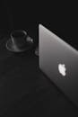 Black and white image showing a laptop and coffee cup in a minimalistic workspace.