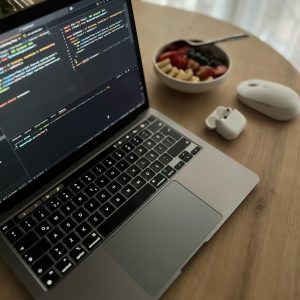 Cozy workspace featuring a laptop, mouse, and healthy fruit bowl on a wooden table.